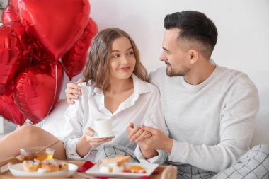 Sevgililer Günü 'nde yatakta kahvaltı eden genç çifte sarılmak.