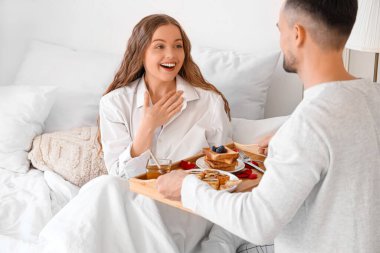 Young man bringing his wife breakfast in bed on Valentine's Day