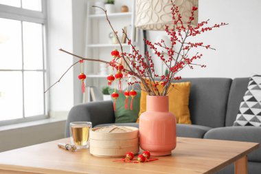 Ağaç dalları olan vazolar, Çin sembolleri ve oturma odasındaki masada bir fincan çay, yakın plan. Yeni yıl kutlaması