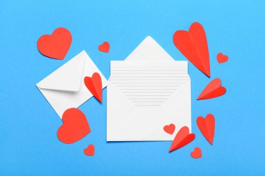 Boş kartlı zarflar ve mavi arka planda kırmızı kağıt kalpler. Sevgililer Günü kutlaması