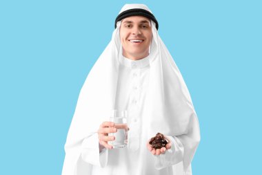 Mavi arka planda hurma ve bir bardak su olan genç Müslüman bir adam. Ramazan kutlaması