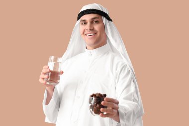 Tarihleri ve bej arka planda bir bardak suyu olan genç Müslüman bir adam. Ramazan kutlaması