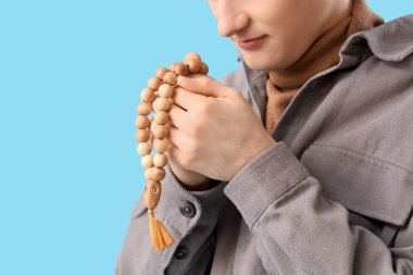 Mavi arka planda tespih çeken genç Müslüman adam, yakın plan. Ramazan kutlaması