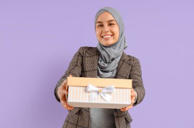 Leylak arkaplanlı hediye kutusu olan genç Müslüman kadın. Ramazan kutlaması
