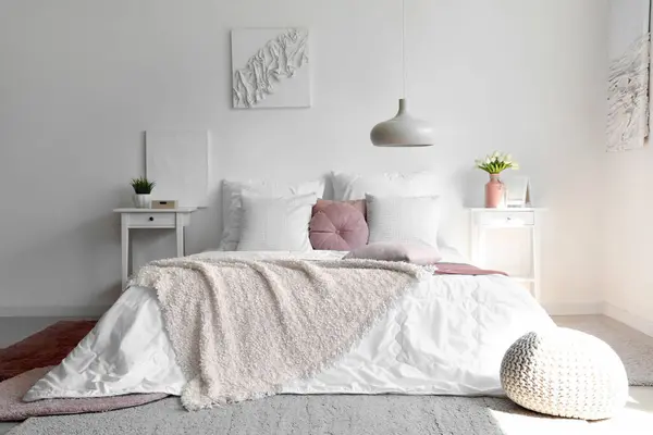 Cozy bed with white blanket and pillows in interior of light bedroom