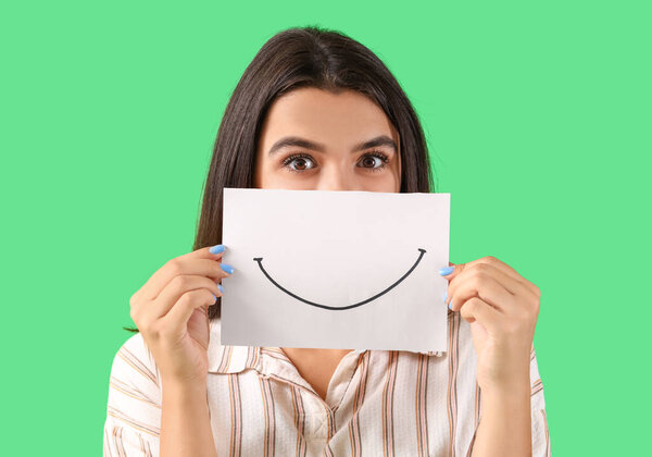 Молодая женщина с бумажной улыбкой на зеленом фоне, крупным планом