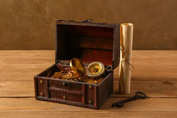 Old chest with coins, compass and map on wooden table near brown wall