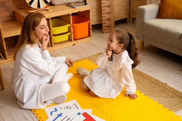 Mature speech therapist working with little girl in office