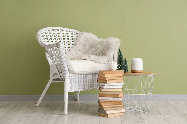 White armchair and cup with marshmallows on stack of books near green wall