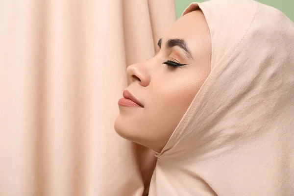 Young African-American Muslim woman with beautiful makeup on green background, closeup