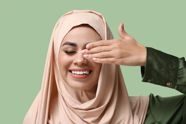 Happy young African-American Muslim woman with beautiful makeup on green background