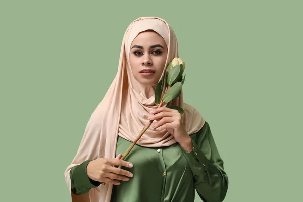 Young African-American Muslim woman with beautiful makeup and flower on green background