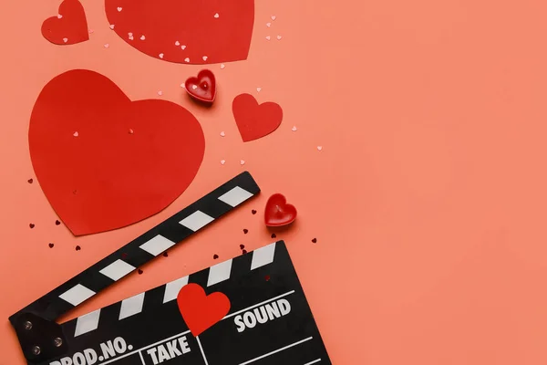 Movie clapper with paper hearts and candles on red background. Valentine\'s Day celebration