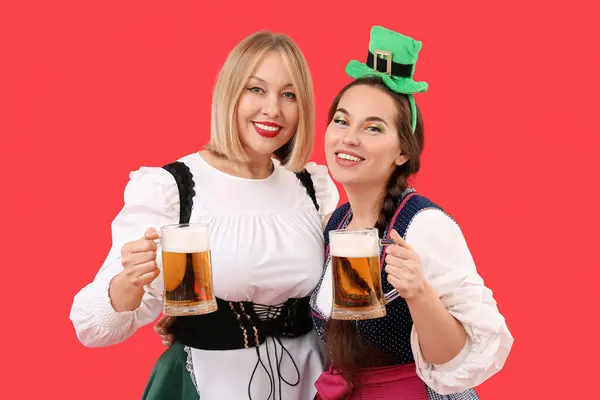 Happy women with beer celebrating St. Patrick\'s Day on red background
