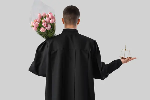 stock image Male judge with tulips and justice scales on light background, back view. International Women's Day celebration