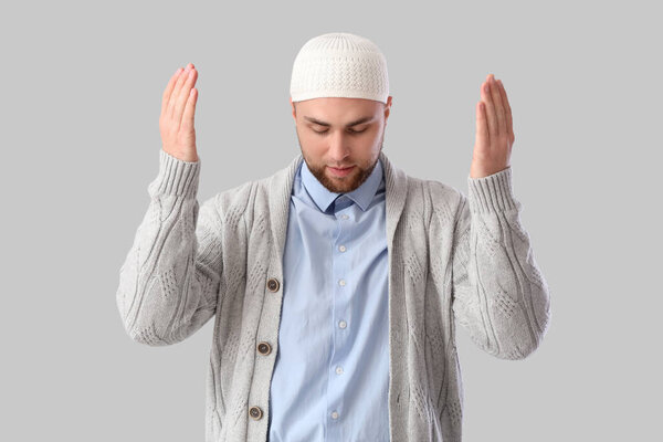 Young Muslim man praying on light background. Ramadan celebration