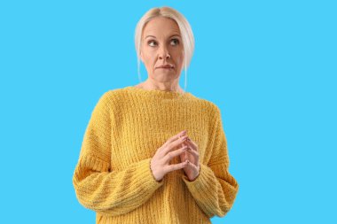 Mavi arka planda düşünceli olgun bir kadın.