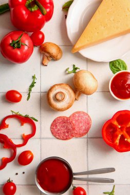 Beyaz fayanslı pizza hazırlamak için farklı malzemeler.