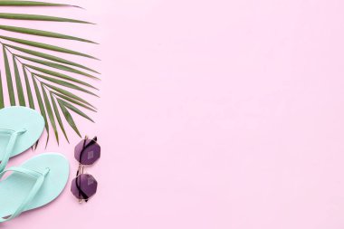 Pembe arka planda şık terlikleri, güneş gözlükleri ve palmiye yaprağı olan kompozisyon