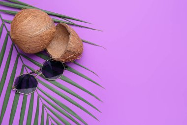 Kompozisyon lezzetli hindistan cevizi, şık güneş gözlükleri ve mor arka planda palmiye yaprağı.