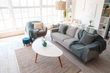 Koltuklu, gri kanepeli ve kahve masalı aydınlık oturma odasının içi.