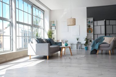 Koltuklu, gri kanepeli ve kahve masalı aydınlık oturma odasının içi.