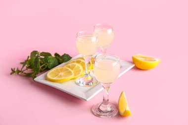 Lezzetli limoncello bardakları ve pembe arka planda dilimlenmiş limon tabağı.