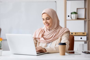 Güzel Müslüman kadın programcı ofiste dizüstü bilgisayar kullanıyor.