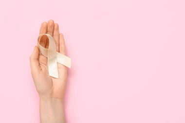 Woman with beige ribbon on pink background. Uterine cancer awareness concept