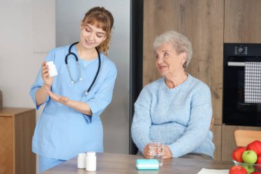 Mutfaktaki yaşlı kadına ilaç şişesini gösteren doktor.