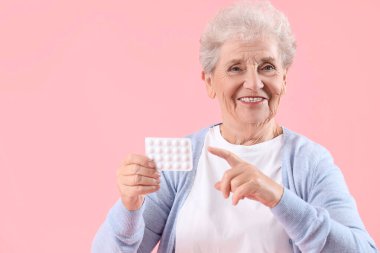 Yaşlı kadın pembe arka planda hapların su topladığını gösteriyor.