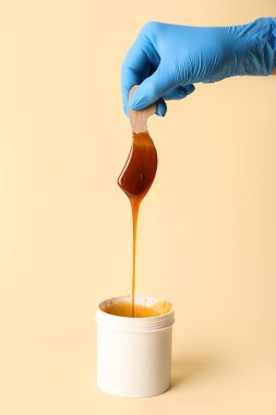 Sarı arka planda şekerleme macunu damlatan bir sopa tutan güzellik uzmanı.