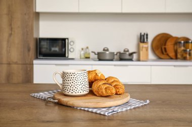 Modern mutfağın ahşap tahtasında bir fincan kahve ve lezzetli kruvasanlar.