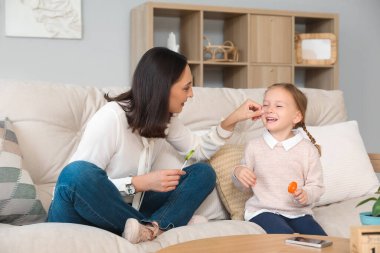 Güzel anne ve tatlı lolipopları olan tatlı küçük kızı evdeki kanepede oturuyorlar.
