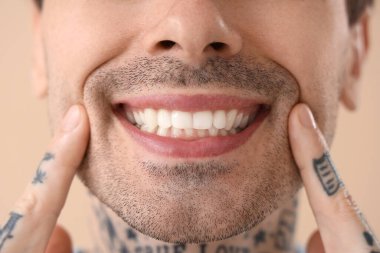 Sağlıklı dişleri olan, bej arkaplan dövmeli genç adam, yakın plan.