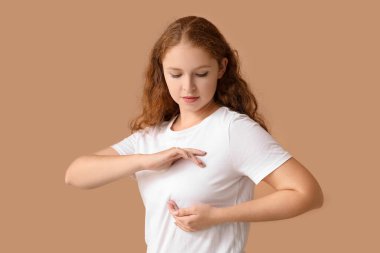 Bej arka planda göğüslerini kontrol eden genç bir kadın. Kanser farkındalığı kavramı