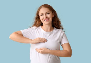 Mavi arka planda göğüslerini kontrol eden genç bir kadın. Kanser farkındalığı kavramı