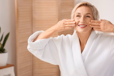 Olgun kadın tuvalette yüz geliştirme egzersizi yapıyor.