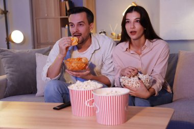 Patates cipsi ve patlamış mısırlı genç çift akşam evde televizyon izliyor.
