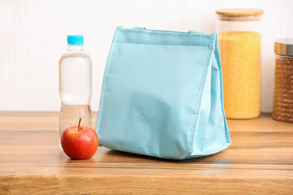 Lunch box bag with apple and bottle of water on table in kitchen