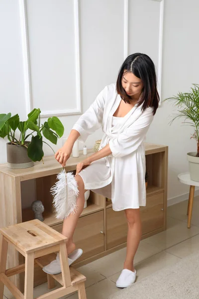Young Asian woman with shaved legs and feather at home