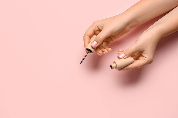 Женские руки с подводкой для глаз на цветном фоне, крупным планом