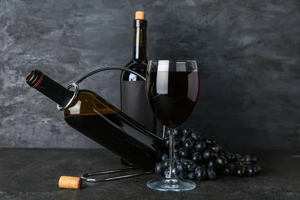 Glass and bottles of exquisite wine with grapes on black background
