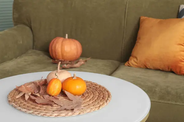 Pumpkins with autumn leaves on table in room