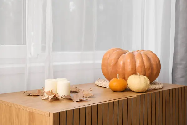 Wooden cabinet with pumpkins, candles and autumn leaves in living room, closeup