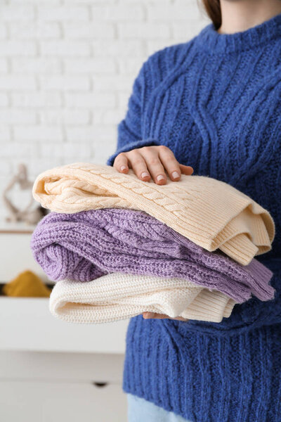 Woman holding different stylish sweaters in room
