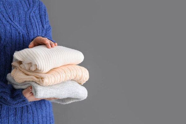 Женщина держит стопку разных стильных свитеров на сером фоне