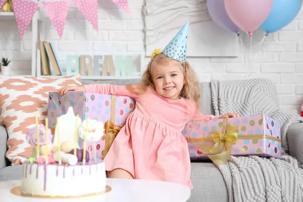 Cute little girl in party hat with gifts celebrating Birthday at home