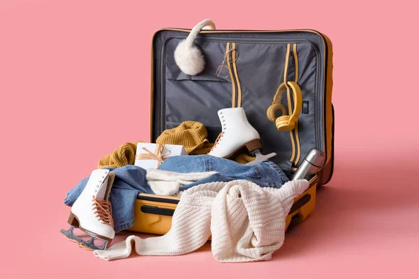 stock image Suitcase with warm clothes, ice skates and Christmas gift box on pink background. Winter vacation concept