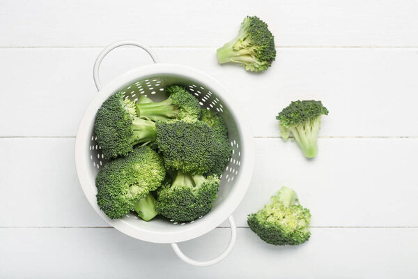 Colander with fresh broccoli cabbages on white wooden background